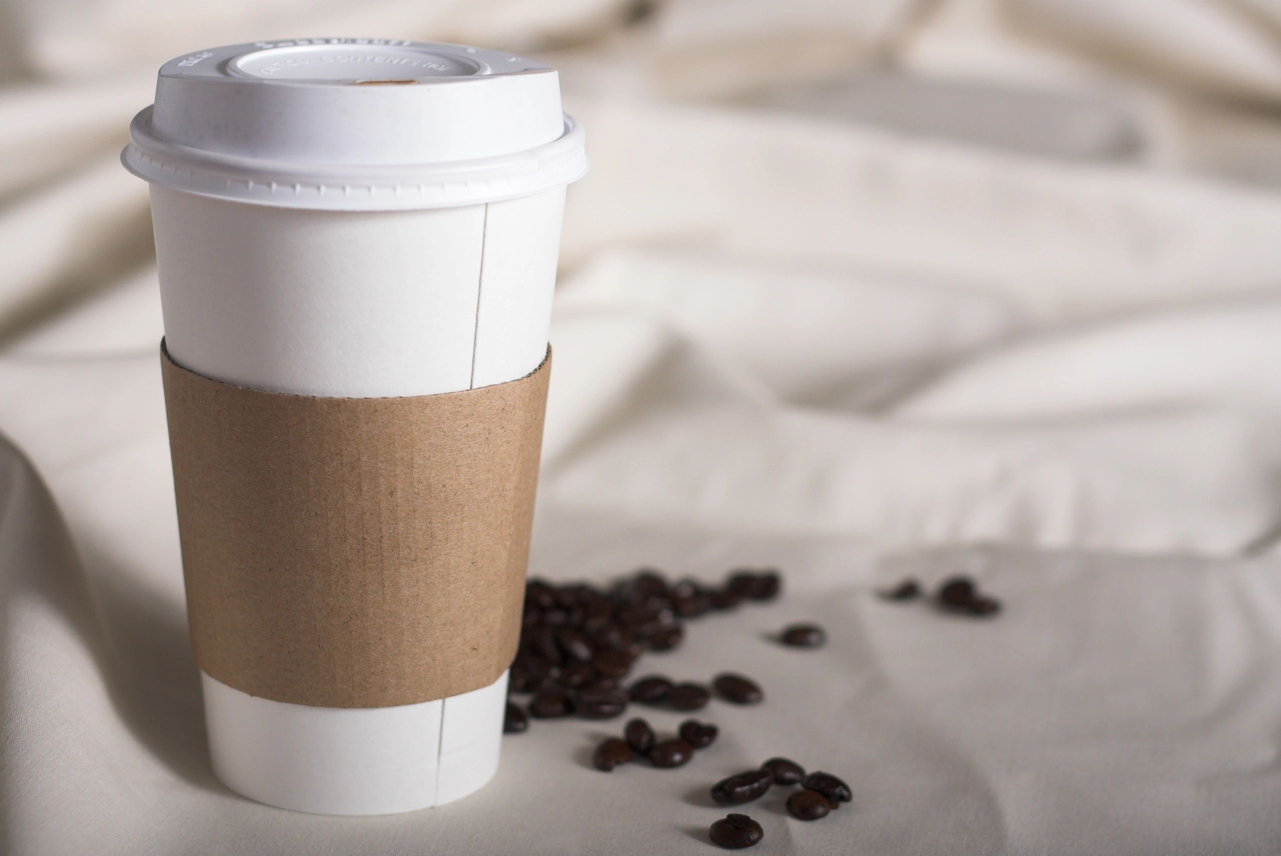 Takeout coffee cup on a table with coffee beans nearby