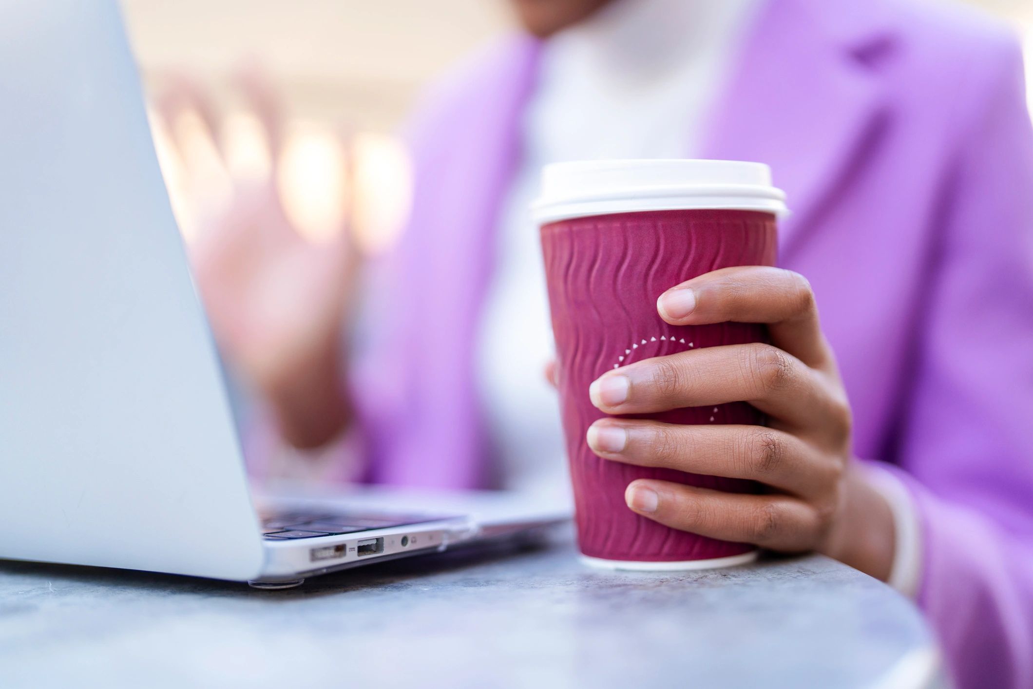 Person holding a coffee cup while working on a laptop in a cafe